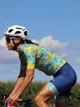 Lade das Bild in den Galerie-Viewer, Frau trägt das Cocoa Radtrikot und Radhose im Hawaii Style Gelb Blau
